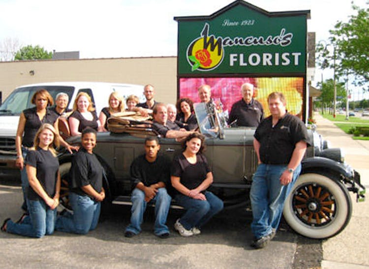 Members of the Mancusos team pose alongside a classic convertible alongside our street sign