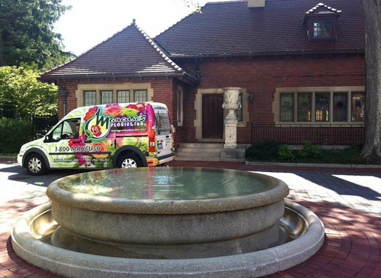 A Mancusos-branded van makes its delivery behind a babbling water fountain